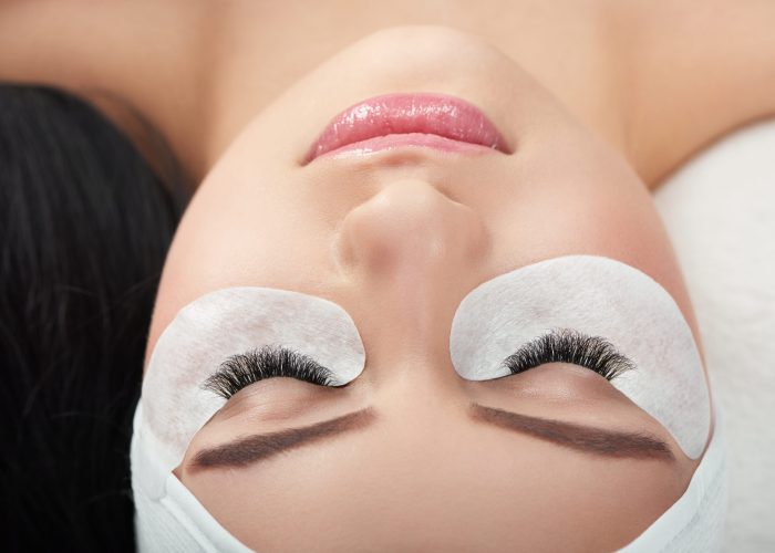 Photo comparison of woman's normal and fake enlarged lashes. Client lying on special coach wearing headbandage for lashmaking. Having black hair. Loving beaty procedures in salone. Pretty young face.